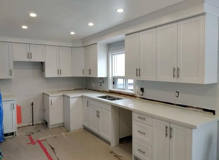 Same kitchen after, white shaker cabinets with quartz counters